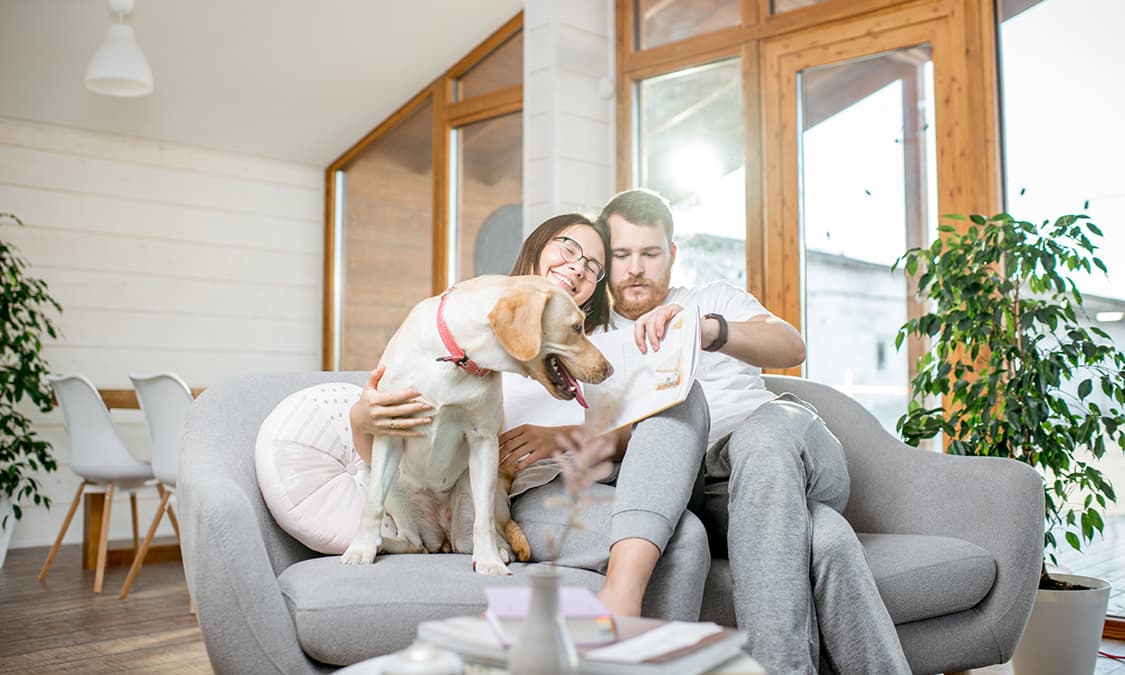 A couple relaxing while sitting on a couch with their dog.